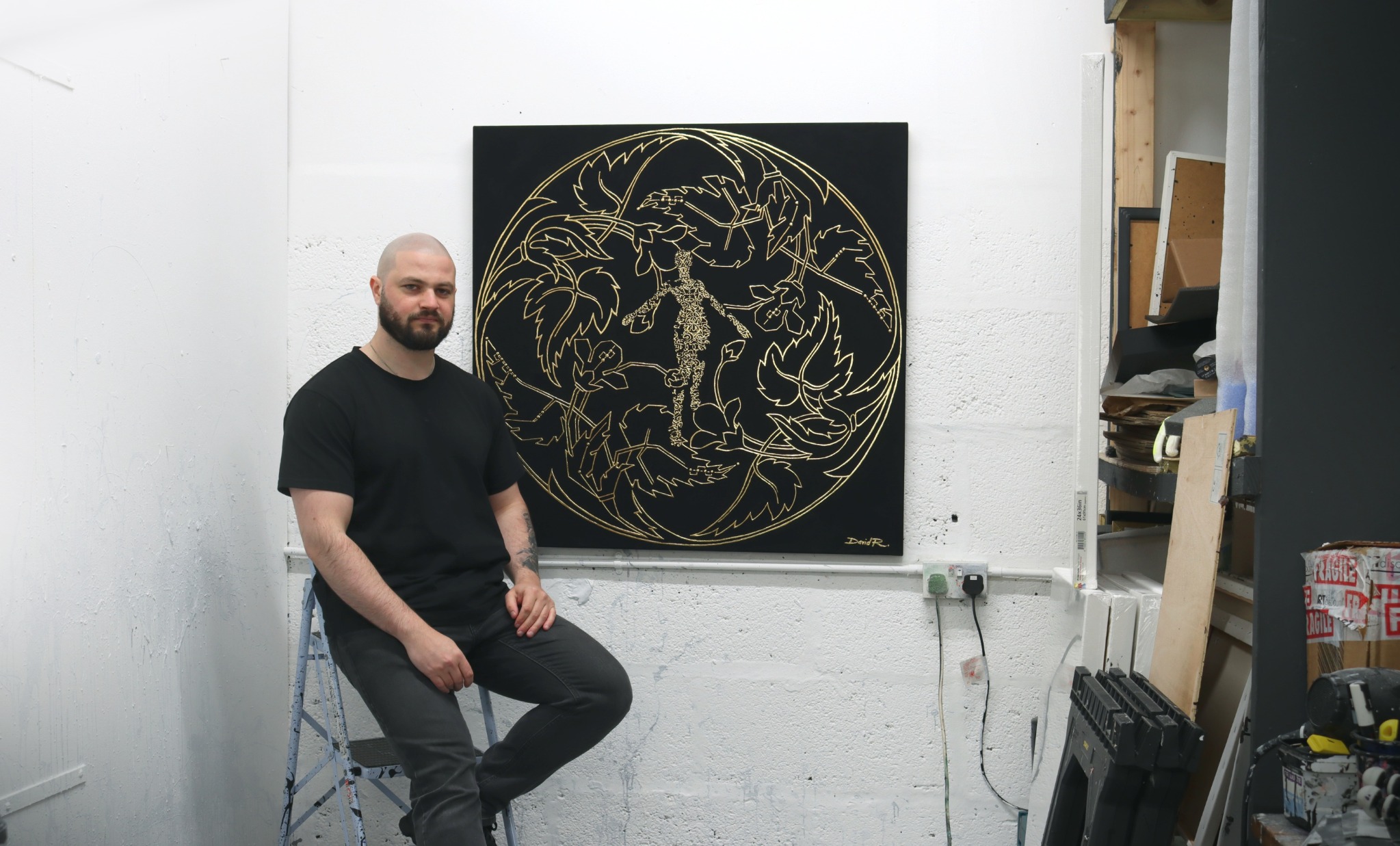 David Roman in his studio beside a black and gold artwork